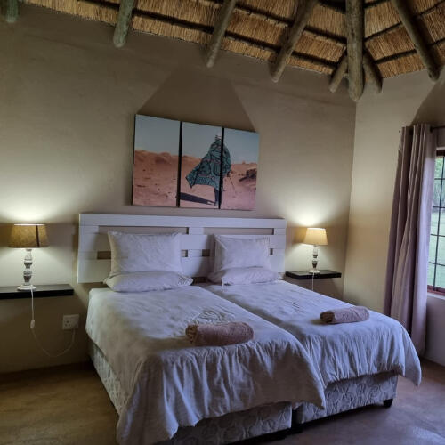 Guest Bedroom at Plain Champagne Guest Farm Twin guest bedroom at Plain Champagne Guest Farm with thatched ceiling, bedside lamps, and garden views